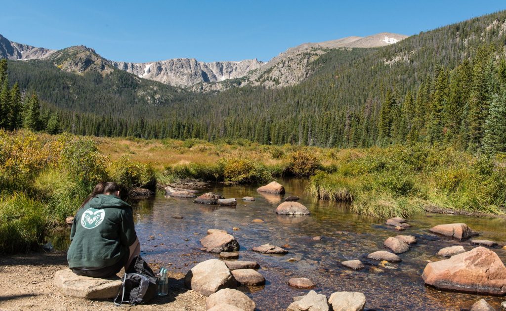 A person sits by a stream in the mountains of Colorado