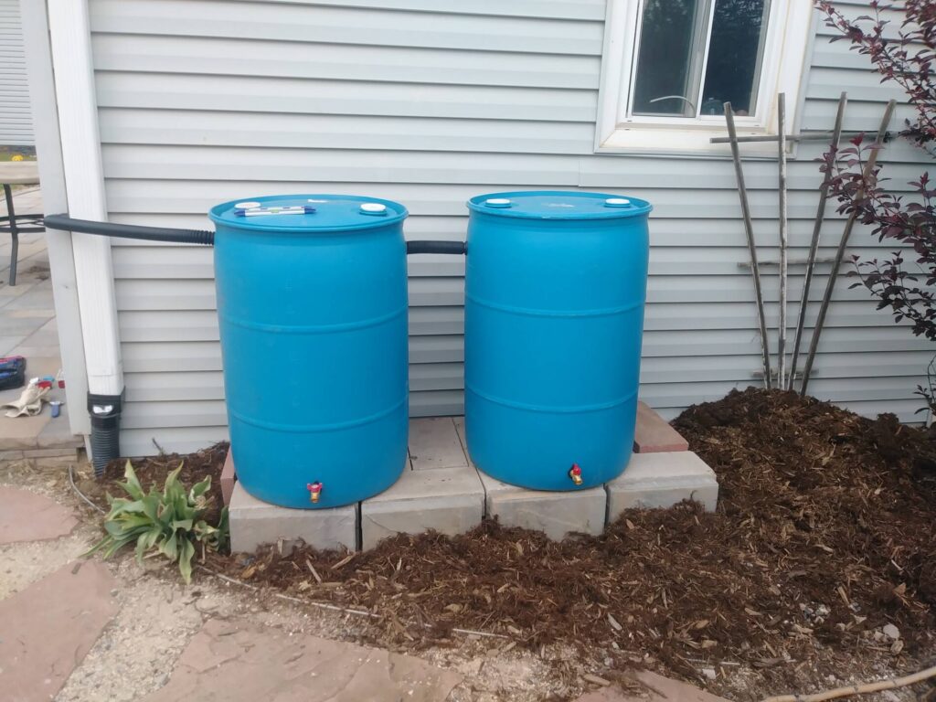 two blue rain barrels sit next to a house