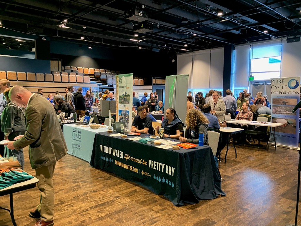 people sit at career fair tables in a large room while others stand to talk and network