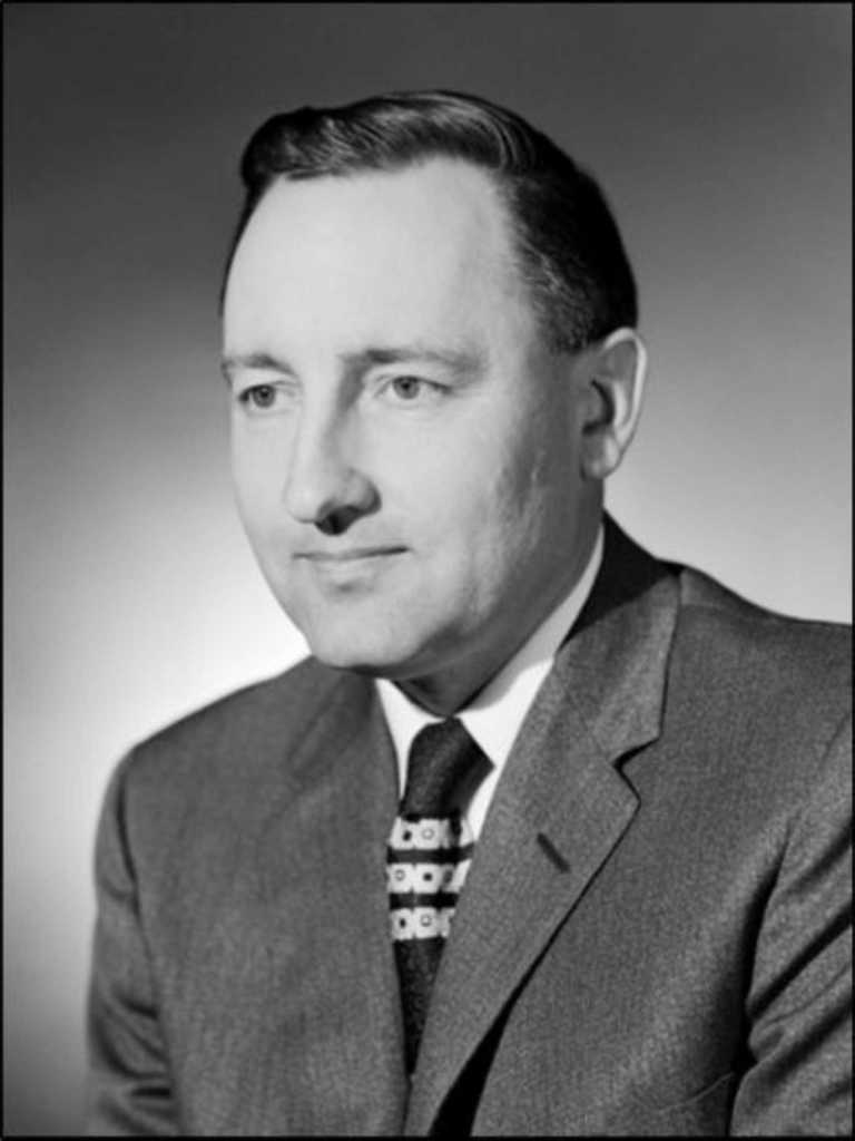 Black and white portrait of Dr. Norm Evans wearing a suit and patterned tie.