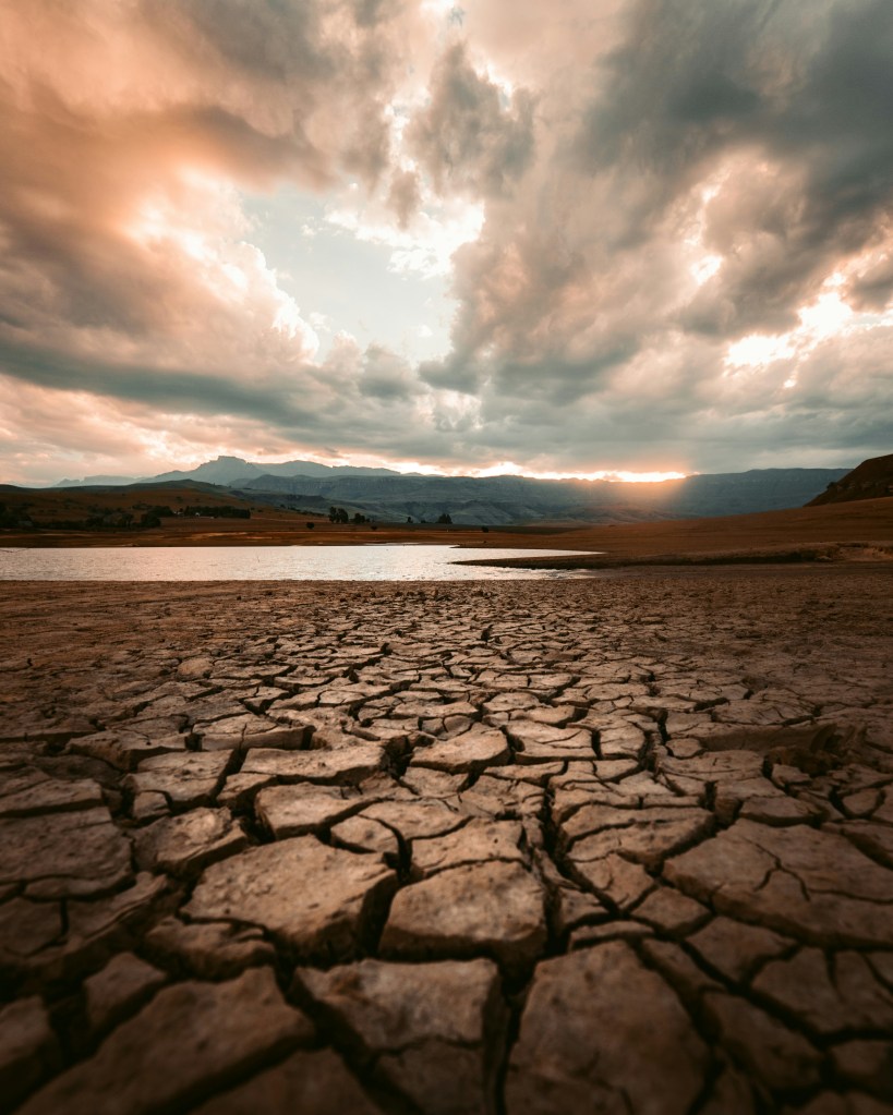 dry, cracked soil with lake and mountains in the background