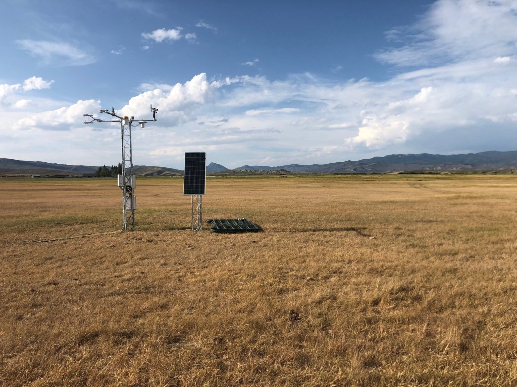 An EC Tower and remote sensing technology stands in an open field with mountains in the background