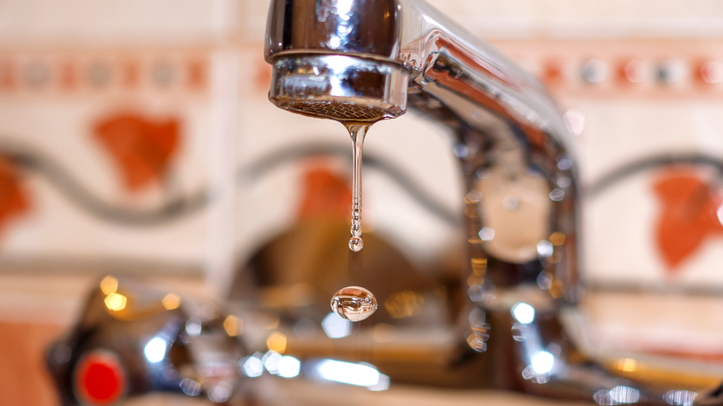 close-up of a silver faucet with a drop of water falling, short depth of field