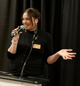 Jolie Brawner speaking at an event with a microphone in hand.