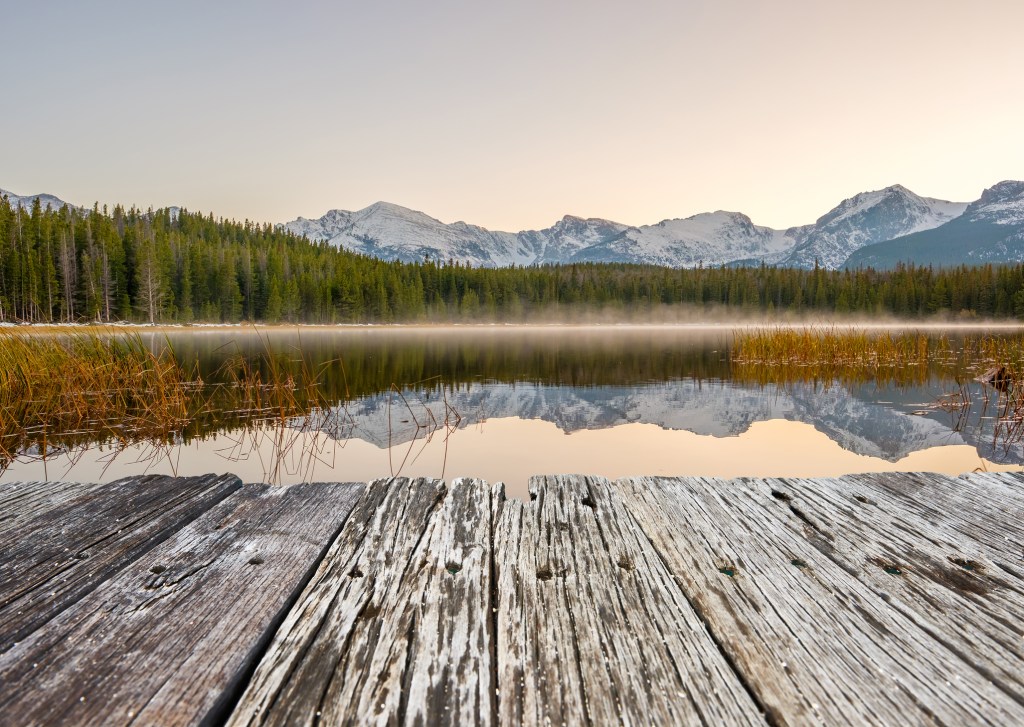 Reflection of snowy rocky mountains in lake with wood dock in foreground