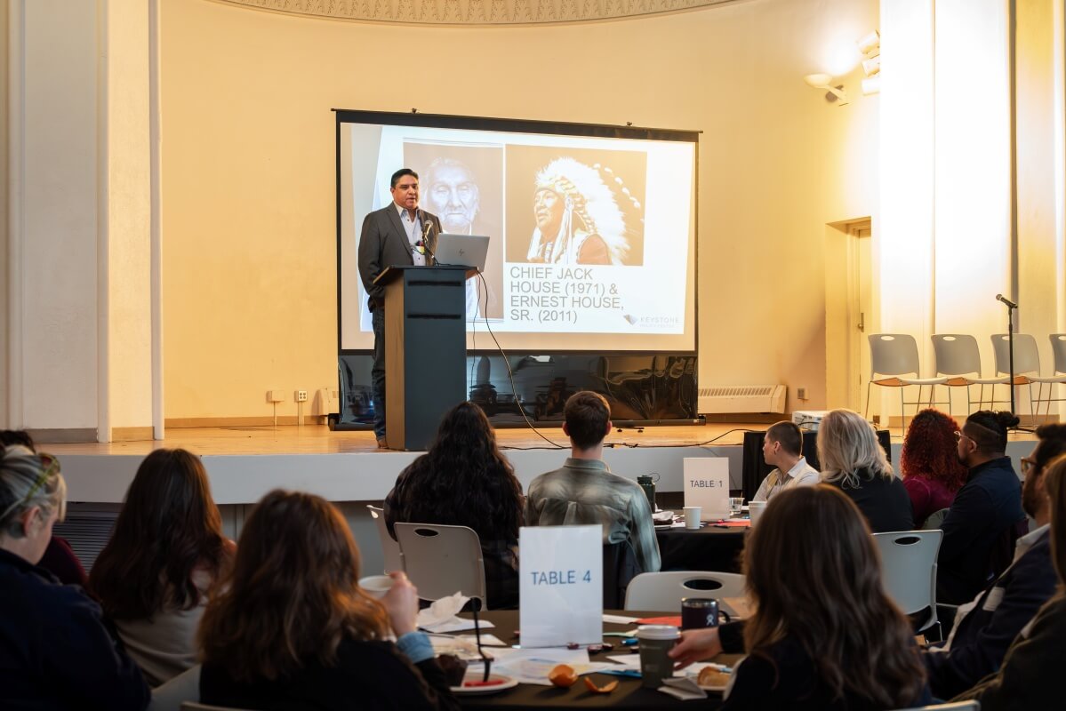 Ernest House Jr. at a podium onstage, delivering his keynote speech, and seated Colorado Water Fellows.