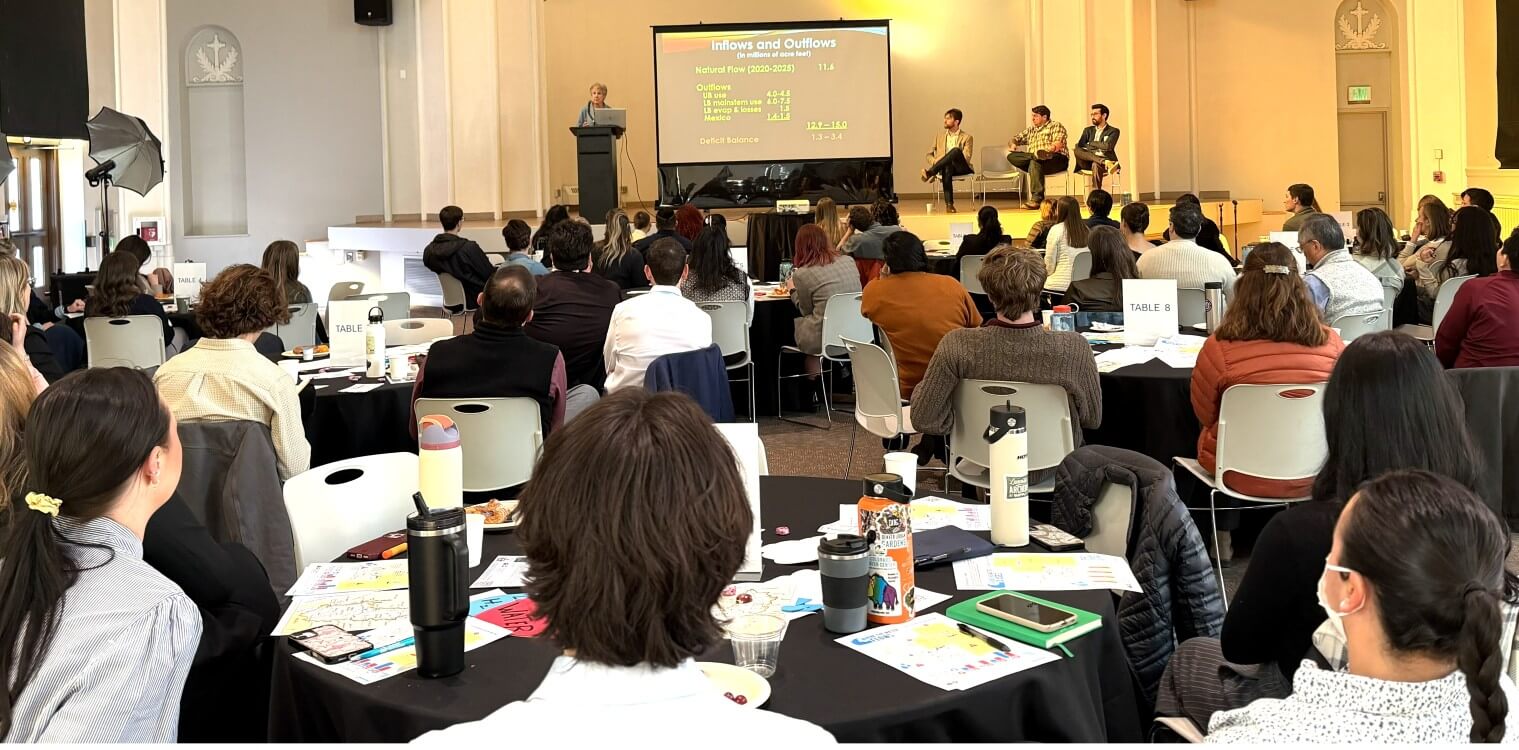 Anne Castle delivering her presentation at a podium onstage, with three other seated panelists onstage to the right and a room full of seated Colorado Water Fellows.