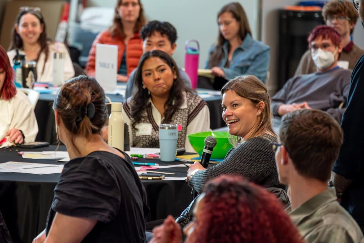 A table of Colorado Water Fellows, with one Fellow holding a microphone and smiling.