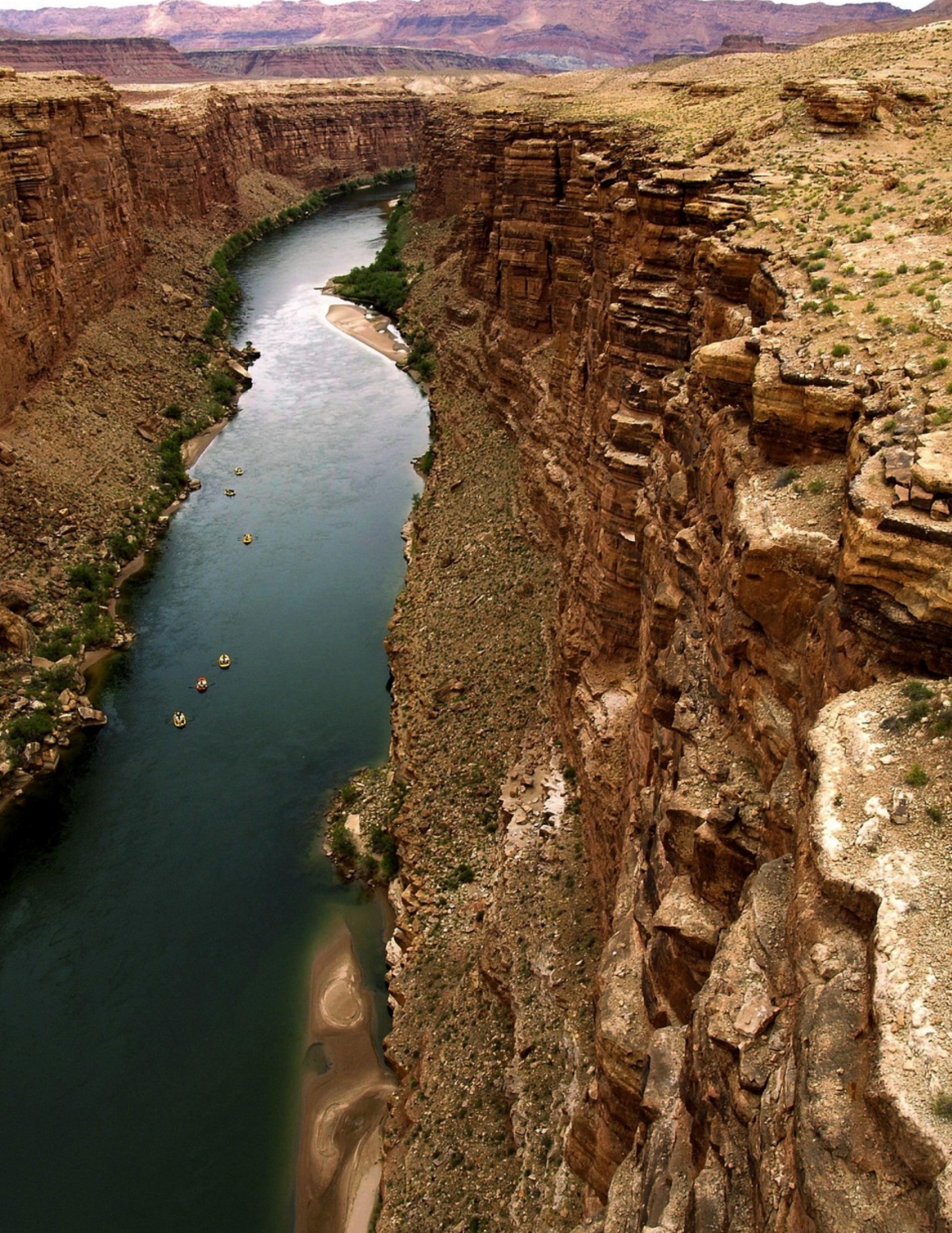 Aerial view of Colorado River flowing through deep canyon with several rafts floating