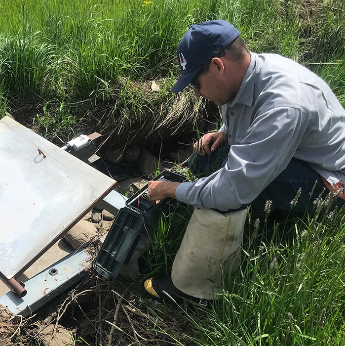 A man in a hat crouches to inspect long range network technology in a grassy field