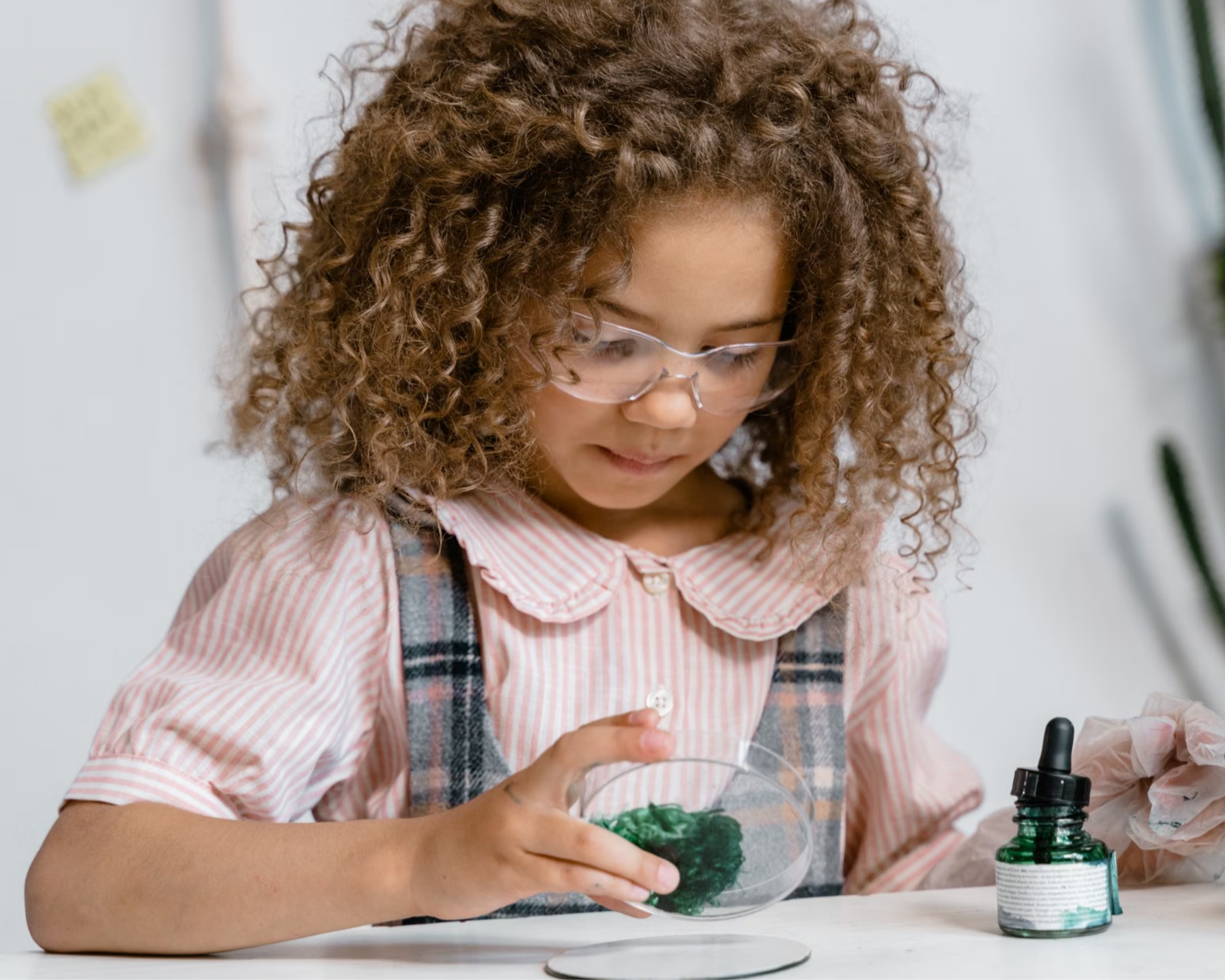 A young girl wearing lab goggles examines contents of a petri dish