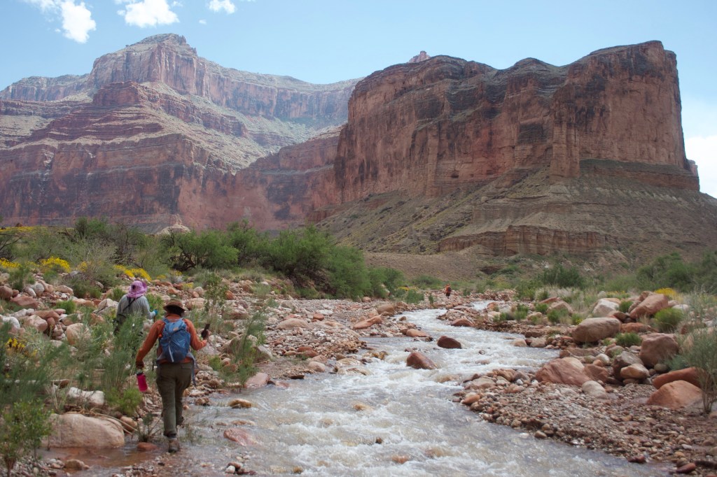 People walk along a river in a desert landscape